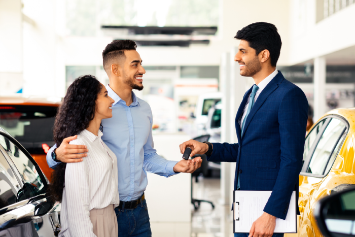 Cheerful man sales associate giving happy young middle eastern couple key from brand new car and smiling