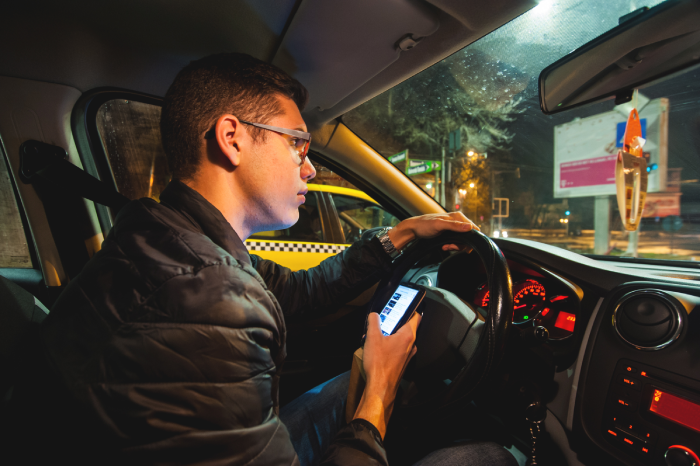 Young driver using his smartphone while driving. Irresponsible teenager texting and driving at night in the city.