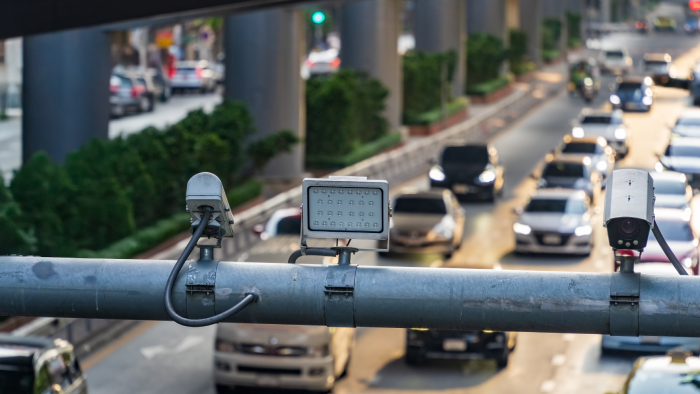 Traffic surveillance cameras monitor busy city road from overhead pipe