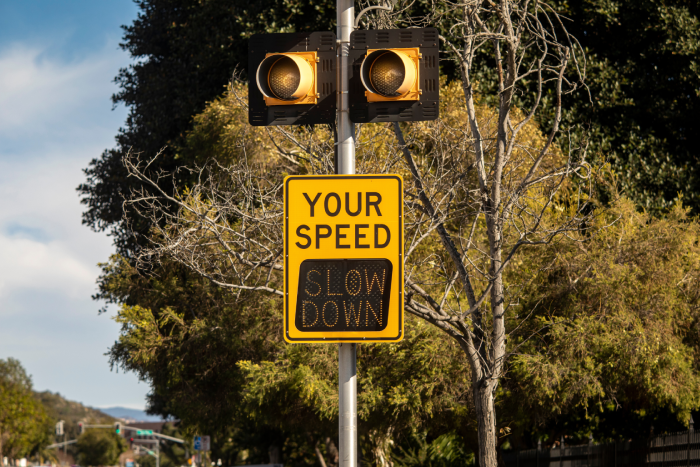 Yellow digital sign measuring traffic speed. The sign says Your Speed and shows Slow Down in digital letters