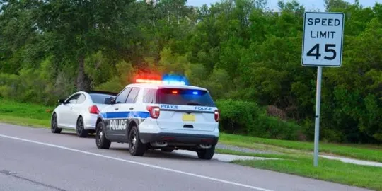 A white police SUV with flashing red and blue lights pulled over behind a white sedan on the shoulder of a paved road.