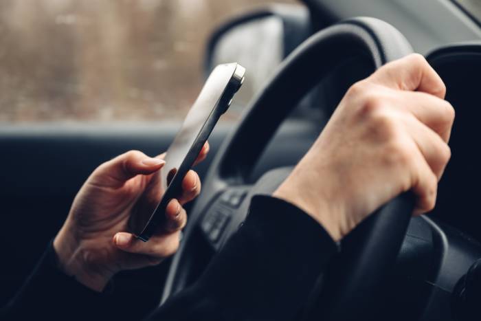 Closeup of female hands typing text message on cell phone while driving car through countryside landscape in winter, selective focus