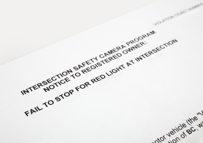Traffic ticket for failing to stop on red light at intersection. Perspective view of traffic infraction notice sent to registered owner. Road safety enforcement or traffic violation.