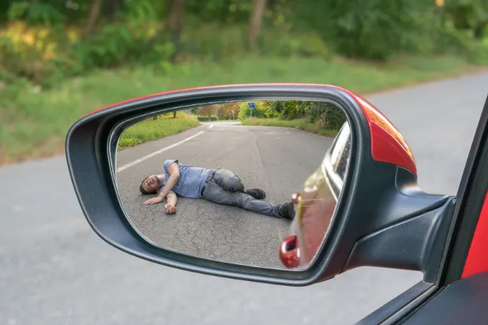 Hit and run concept. View on injured man on road in rear mirror of a car.