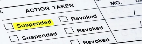 A close-up, angled shot of a legal or official document under the heading "ACTION TAKEN." The word "Suspended" is highlighted in bright yellow next to a checkbox, with other options like "Revoked" visible in the list.