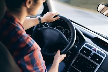 The image shows a high-angle, over-the-shoulder view of a man driving a car on an open road.